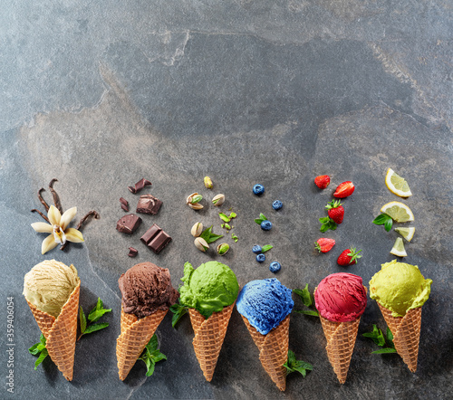Set of various colorful ice creams in waffle cones with fruits slices on the grey background.