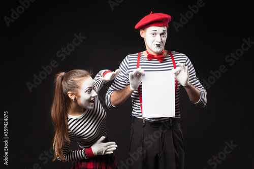 Two mimes man and woman present white paper on isolated black background