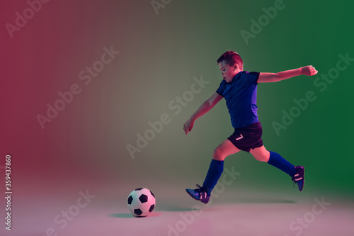 Attacking. Teen male football or soccer player on gradient background in neon light. Caucasian boy training, practicing on the run, in jump. Concept of sport, competition, winning, motion, action.