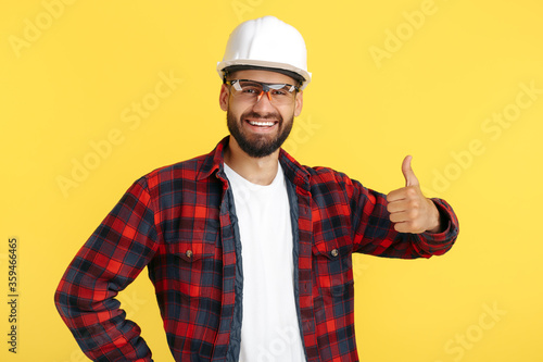 Handsome bearded engineer or constructor man in casual outfit show good gesture over yellow background.