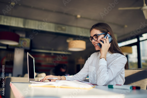 Attractive female administrative manager of restaurant arranging working meeting with staff members to discuss plans for month through telephone conversation sitting in food court using technology