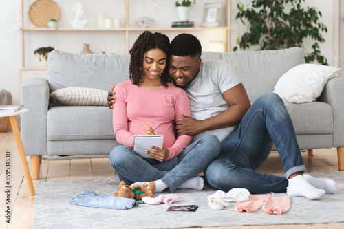 Beautiful pregnant family preparing baby clothes and making list