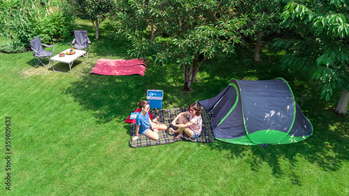 Aerial top view of campsite from above, mother and daughter having fun, tent and camping equipment under tree, family vacation in camp outdoors concept 