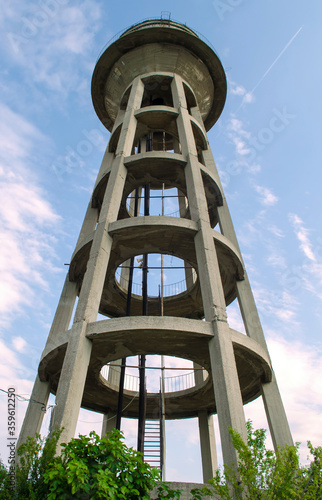 Abandoned pumping station. Water tower of concrete and wood, metal stairs and railings. Down the spiral staircase. Art curve stair with a few rainning. Clear blue sky.