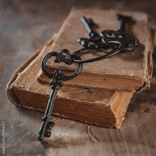 old vintage keys on an old battered book, wooden background.