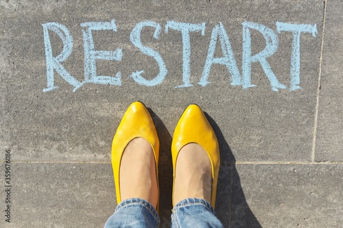 Restart concept, top view on woman legs and text written in chalk on gray sidewalk