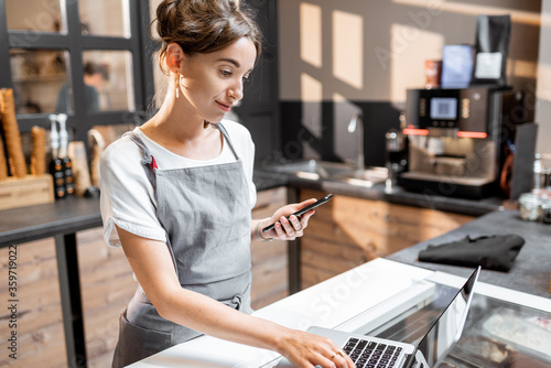 Young saleswoman working with laptop at the counter in ice cream shop or cafe. Concept of a small business and retail