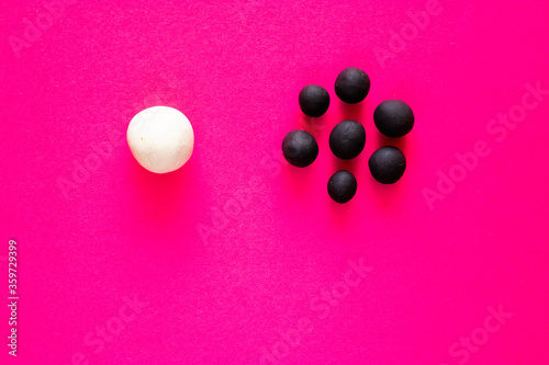 Large white ball separated from many smaller black balls. Plasticine toys, concepts of racism, white privilege and diversity. Pink vibrant backgrounds representing female racism