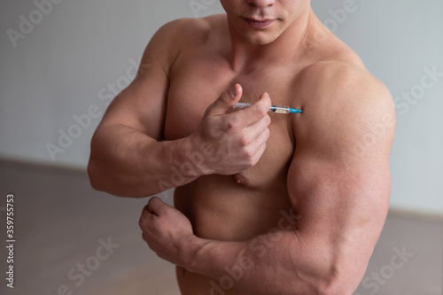 A muscular man with a naked torso holds a dope syringe. Unrecognizable bodybuilder puts himself steroids. Athlete cheats for gaining muscle mass.