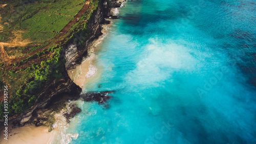 Aerial photo from airplane of a wonderful landscape island with clean sandy shore. Rock cliff on dreamland Bali beach with beautiful blue color of sea water. Background with copy space for website