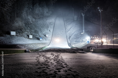 Ski jump at night illuminated by lights covered with snow. Winter sport season. Wide shot, looking up