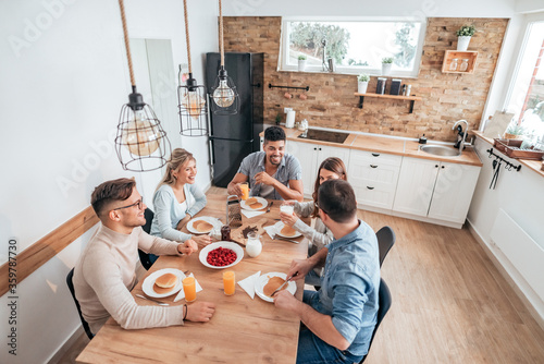 People and holidays concept. High angle image of five young people eating homemade pancakes in cozy apartment.