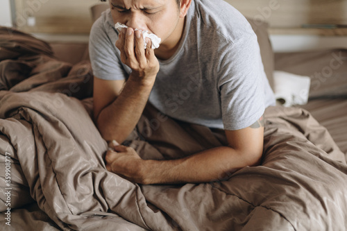 Young man with a cold blowing her runny nose with tissue. Asian man get sick sneezing from flu. Healthcare and medical concept.