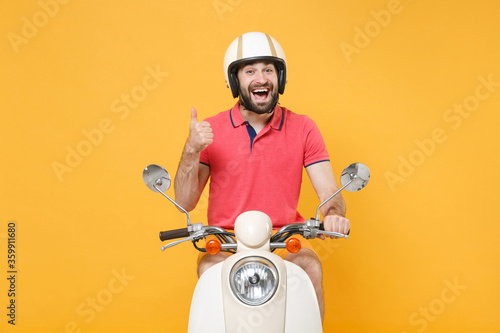 Cheerful young bearded guy in casual summer clothes helmet driving moped isolated on yellow background studio portrait. Driving motorbike transportation concept. Mock up copy space. Showing thumb up.