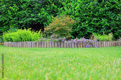 A wooden log roll edging between a grass lawn and a shrub border.
