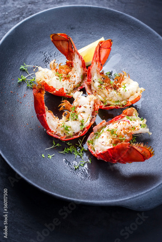 Traditional barbecue spiny lobster tail sliced and offered with lemon slice and herbs as closeup on a modern design plate