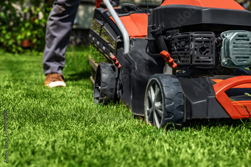 A man moves with a lawn mower and mows green grass. Garden care concept