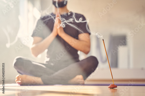 Young man practicing yoga in studio with incense stick