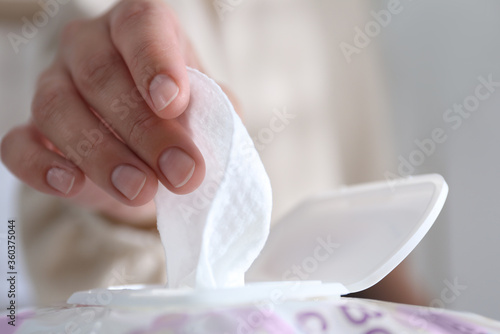 Woman taking wet wipe out of pack against blurred background, closeup