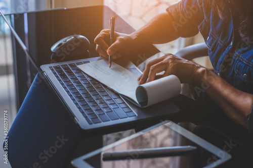 Business woman hand writing and signing white blank bank cheque book with laptop computer, mouse and digital tablet on the desk at office. Payment by check, paycheck, payroll concept. 