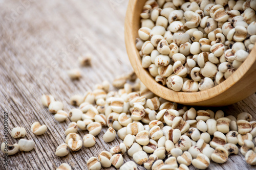 White Job's tears ( Adlay millet, pearl millet or coix seeds ) in wooden bowl isolated on wood table background. 