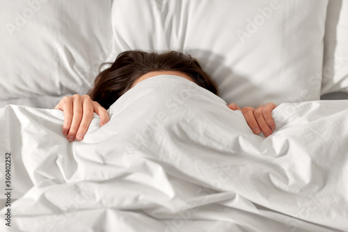 people, bedtime and rest concept - woman lying in bed under white blanket or duvet