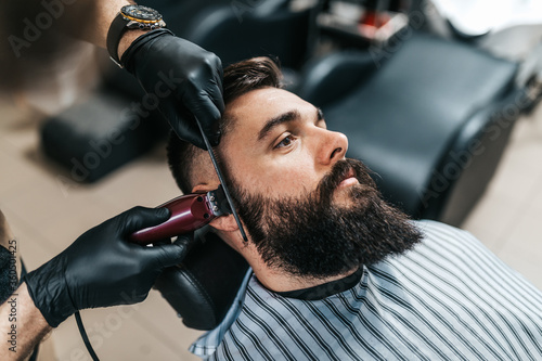 Young good looking man visiting barber shop. Trendy and stylish beard styling and cut.