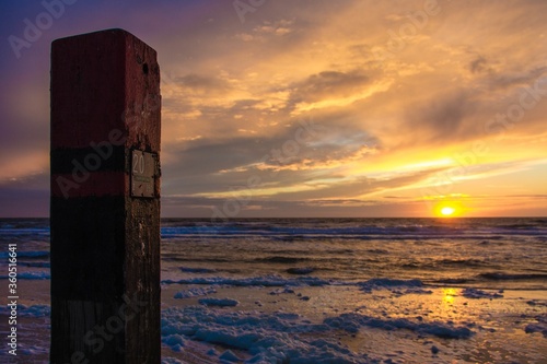 Beautiful shot of a sunset in Dutch Island of Texel beach with beach pole and foam on the sand