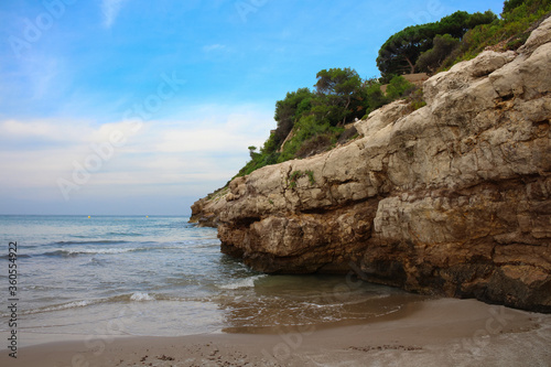 Rock with trees on the sandy beach of Salou against the blue sky. Spain.