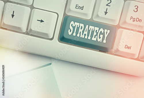 Conceptual hand writing showing Strategy. Concept meaning action plan or strategy designed to achieve an overall goal White pc keyboard with empty note paper above white key copy space