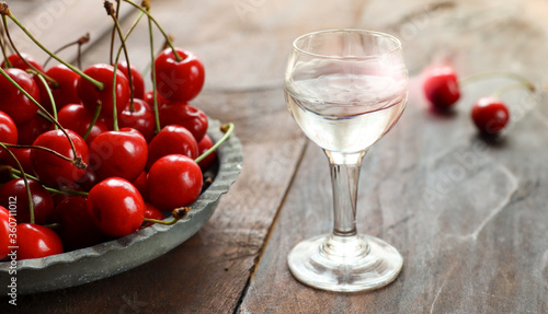 Kirsch or Kirschwasser - a strong alcoholic cherry drink in a glass and fresh cherry on an old dark wooden table