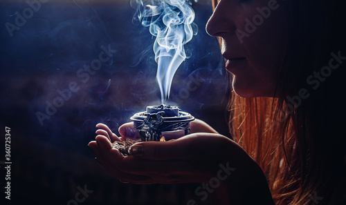 incense in a woman hand, incense smoke on a black background.