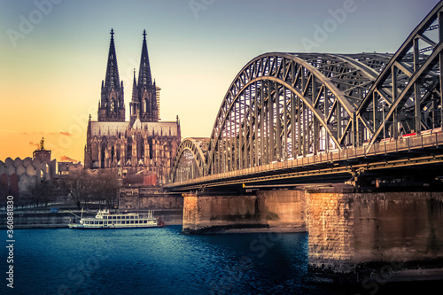 Cologne, Germany - UNESCO Cathedral in Cologne Germany and Hohenzollern Bridge across Rhine River with Boat at Evening Sunset