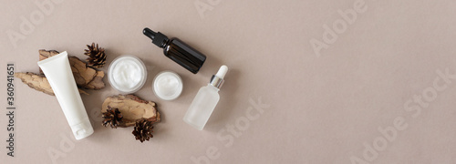 Hand, eye, facial moisturizer cream, serum, essential in glass bottles and pine bark and cone on beige background flat lay, top view. Set for skin and body care beauty products banner format