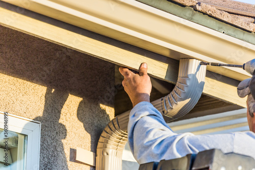 Worker Attaching Aluminum Rain Gutter and Down Spout to Fascia of House