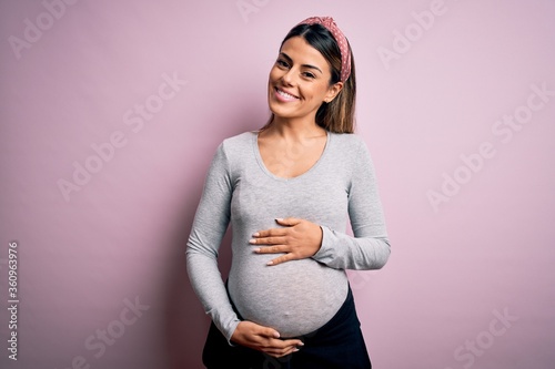 Young beautiful brunette woman pregnant expecting baby over isolated pink background with a happy and cool smile on face. Lucky person.