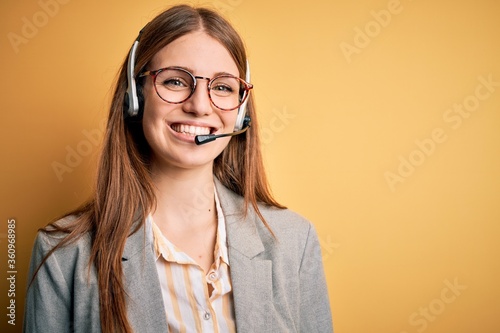 Young redhead call center agent woman overworked wearing glasses using headset with a happy and cool smile on face. Lucky person.