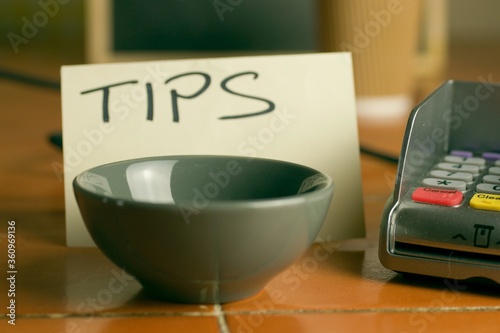 Closeup shot of a bowl near a contactless pdq machine and a tips note leaning on a coffee cup