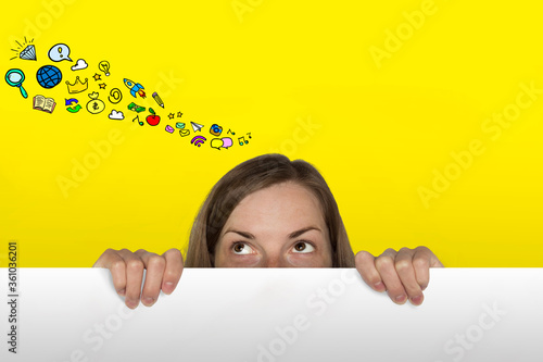 Girl Looks out from behind the White Paper Sheet on the Yellow Background. Added Icons in Wish Desires. Dream Girl Concept.