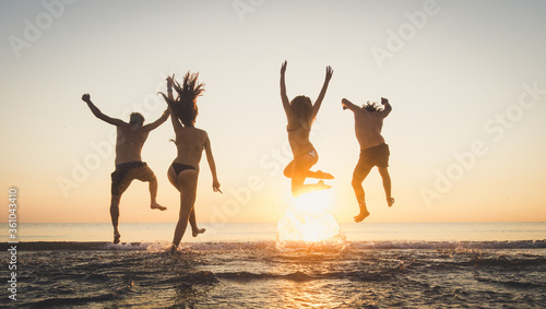 Group of happy friends running and jumping in the sea at sunset. Young people enjoy holiday vacation at the beach.