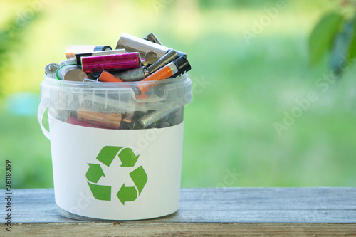 Battery recycle bin with old element on wood table on green grass background