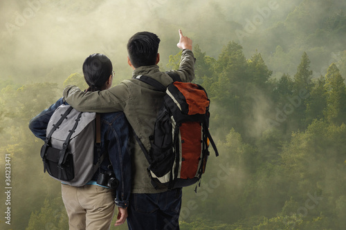  Travelers couple with the backpack on the top of mountain in the green forest and enjoy the beauty of landscape, Adventure and travel in the mountains region concept