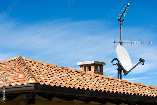 Closeup of a Television Aerial and Satellite Dish on the House Roof on blue sky with clouds