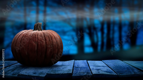 One spooky halloween pumpkin blank template on a wooden bench with a misty forest night background with space for product placement.