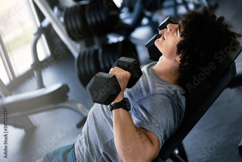 Muscular man working out in gym doing exercises with dumbbells at biceps