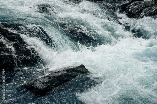 Big rapids of powerful mountain river. Beautiful background with azure water in fast river. Frozen motion of tall mountain river rapids. Power majestic nature of highlands. Backdrop of aqua turbulence