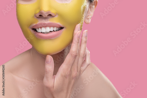 Woman applying novel golden face mask to her skin