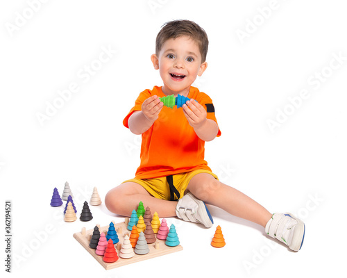 A beautiful European boy plays with wooden Montessori toys on a white background. Child 2.5 years old. Montessori pedagogy, didactic materials. Development and training of preschool children.