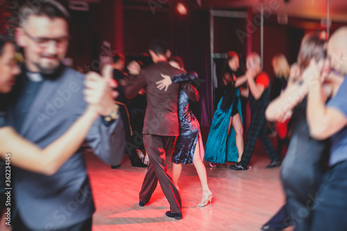 Couples dancing argentinian dance milonga in the ballroom, tango lesson in the red lights, dance festival