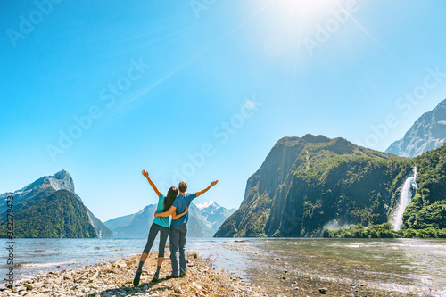 Outdoor couple happy with arms outstretched in Milford Sound New Zealand in nature enjoying active outdoor lifestyle hiking in Milford Sound, New Zealand by Mitre Peak in Fiordland.